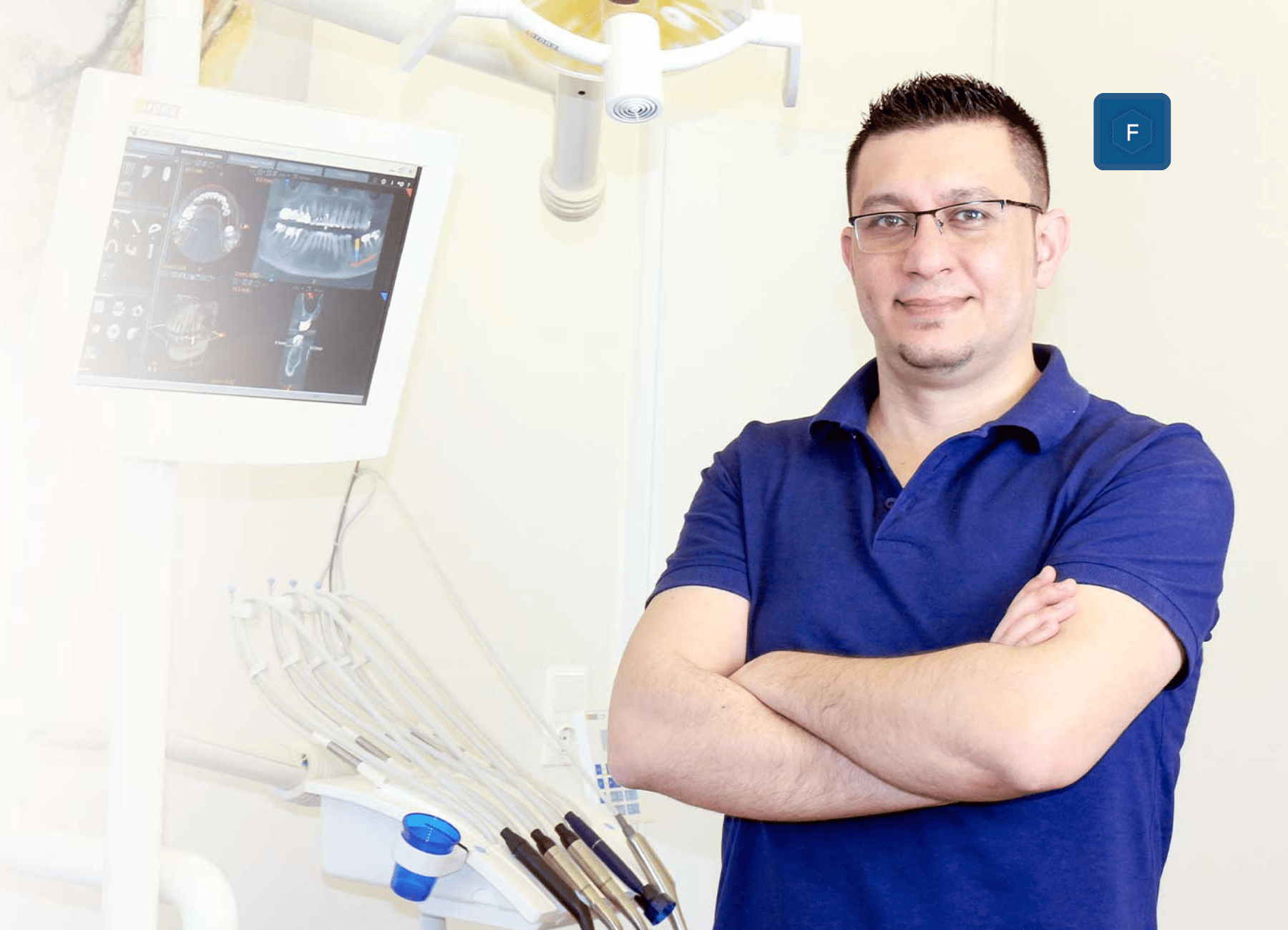 Eine Person mit Brille und blauem Poloshirt steht selbstbewusst mit verschränkten Armen in einer Zahnarztpraxis. Hinter ihr zeigen zahnärztliche Geräte und ein Röntgenmonitor Kieferbilder und verdeutlichen damit die Präzision und Kompetenz, mit der Zahnärzte ihre Patienten täglich behandeln.
