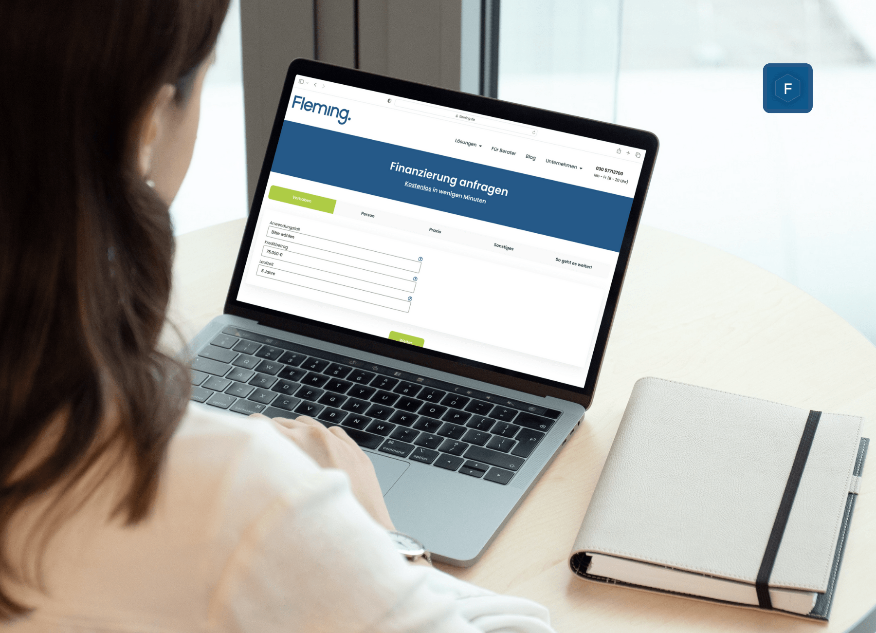 Eine Person sitzt an einem Tisch in einer Zahnarztpraxis und arbeitet an einem Laptop. Auf dem Laptop ist eine Webseite geöffnet, auf der ein Formular mit dem Titel „Finanzierungsanfragen“ angezeigt wird. Auf dem Tisch liegen ein Notizbuch und ein Stift.