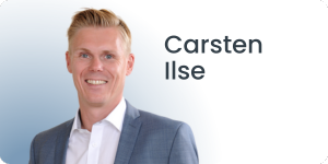 Eine Person in hellblauem Anzug und weißem Hemd lächelt vor einem blau-weißen Hintergrund mit Farbverlauf. Daneben steht der Name Carsten Ilse.