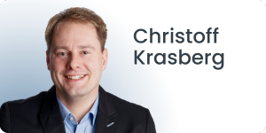 Eine Person im Anzug, die lächelt. Daneben steht auf hellem Hintergrund der Name „Christoff Krasberg“.