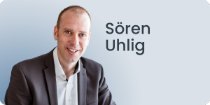 Vor hellblauem Hintergrund lächelt ein Mann im Anzug in die Kamera. Neben ihm steht Sören Uhlig.
